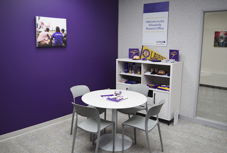 Seating area in front of a bookshelf with Laurier-branded merch and a sign that says 'Welcome to the Yellowknife Research Office'.