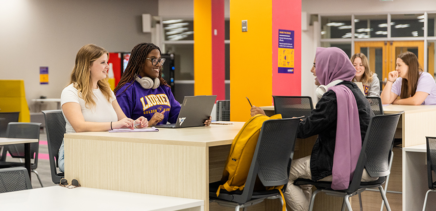 Students sitting at a desk chatting while they study in One Market