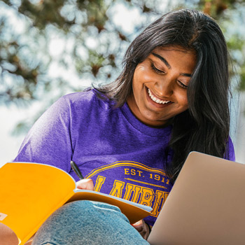 female student in purple Laurier shirt writing in yellow notebook