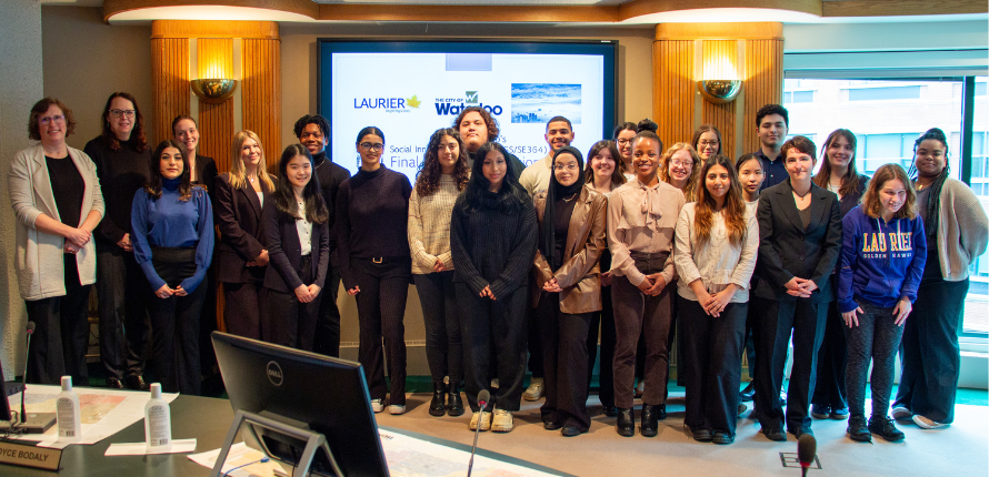 Group photo of the mayor and Laurier president with a large group of students in front of a presentation screen